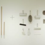 A minimalist flat lay of various cleaning tools arranged on a white wall, showcasing a modern concept.