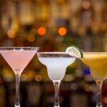 Vibrant cocktails lined up beautifully on a bar counter with a blurred background.