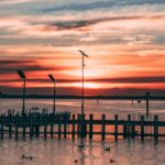 A breathtaking sunset view over a calm sea with a pier and ducks in silhouette.
