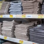 Neatly folded towels in various colors stacked on retail shelves inside a store.