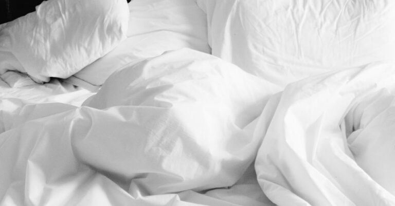 A cozy, rumpled white bed with soft sheets and pillows in a modern bedroom setting.