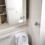 A contemporary bathroom with a toilet, sink, and storage shelves featuring a minimalist design.