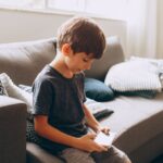 Young boy engaging with phone on couch in sunny, modern living room.