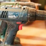 A row of cordless power drills on a wooden workbench, ready for use.