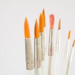 Close-up of assorted paintbrushes with orange bristles on a white background.