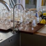 Glassware and colorful cups drying by a kitchen sink with bright natural light.
