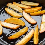 Freshly fried golden potato wedges sizzling in a cast iron skillet, showcasing delicious homemade cooking.