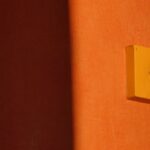 Minimalist image showcasing a light switch casting shadows on a vibrant orange wall.