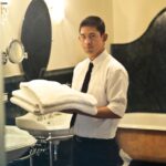 A hotel employee holding towels in a luxury bathroom with elegant decor.