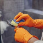 Crop faceless male in orange rubber gloves wiping by sponge shower nozzle