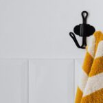A striped yellow and white towel hangs on a wall-mounted hook in a minimalist setting.