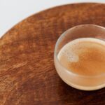 From above of coffee with thin froth in glass cup placed on small round wooden table on white background