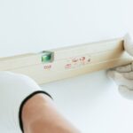 Hands in white gloves using spirit level on wall for precise leveling.