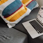Elegant gray sofa setup with a laptop and colorful throw pillows for a cozy workspace.