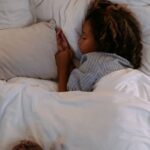 A young girl peacefully sleeping under soft, white bedding with a plush owl nearby.