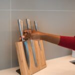 A person retrieving a knife from a wooden kitchen block on a countertop.