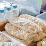 Plastic-wrapped food items and bottled water organized in storage containers and tin cans.