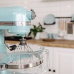 A close-up of a blue stand mixer in a sleek, modern kitchen setting.
