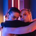 Two models in neon-lit studio embracing with bold glitter makeup