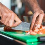 Close-up of a chef slicing fresh tomatoes on a green cutting board in a modern kitchen.