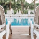 Relaxing view of empty poolside sunloungers amidst palm trees, perfect for summer vacations.