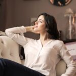 A serene woman enjoys a moment of reflection on a luxurious vintage sofa in a well-designed interior.