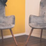 Two contemporary gray armchairs in a minimalist interior with a yellow accent wall and wooden flooring.