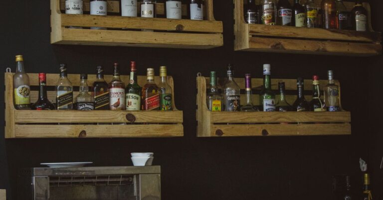 A rustic wooden shelf display of liquor bottles on a dark wall, perfect for a bar setting.