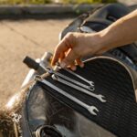 Close-up of a man's hand arranging wrenches on a motorcycle seat outdoors.
