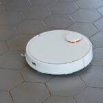 A sleek, white robotic vacuum cleaner operating on a hexagonal tiled floor.